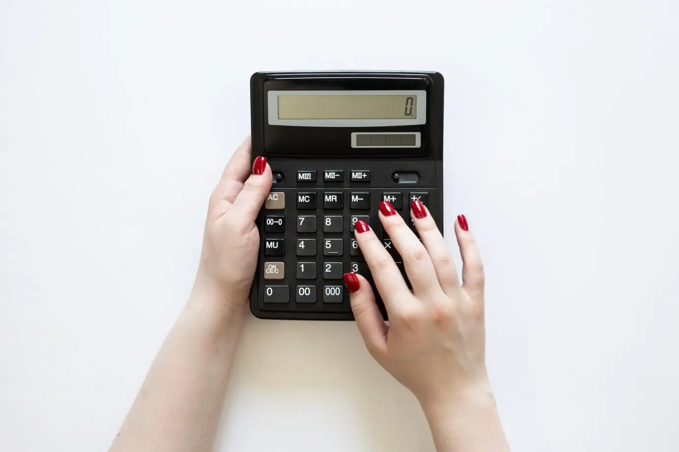 Вид сверху: женщина держит в руках черный калькулятор на белом фоне.