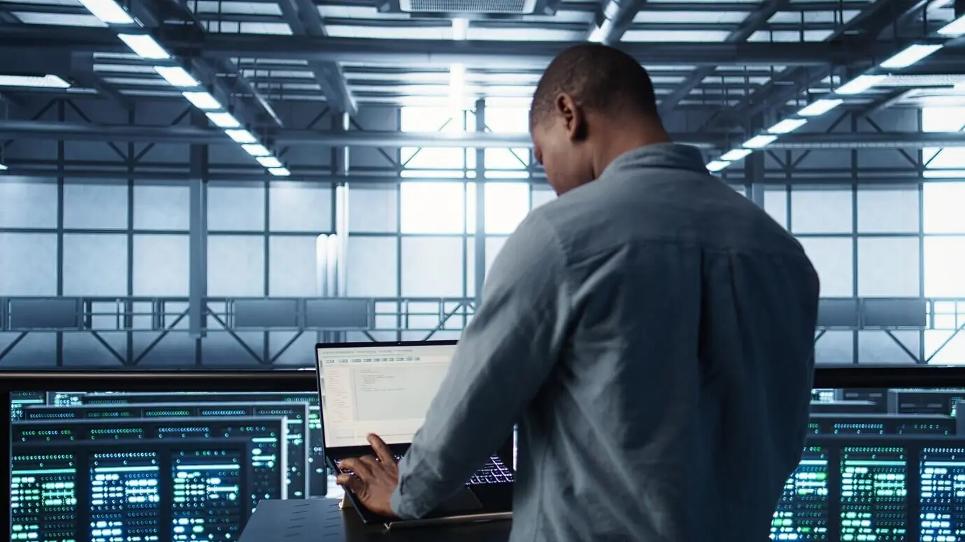 Мужчина программирует в дата-центре, тестируя сценарии аварийного переключения с помощью ноутбука.