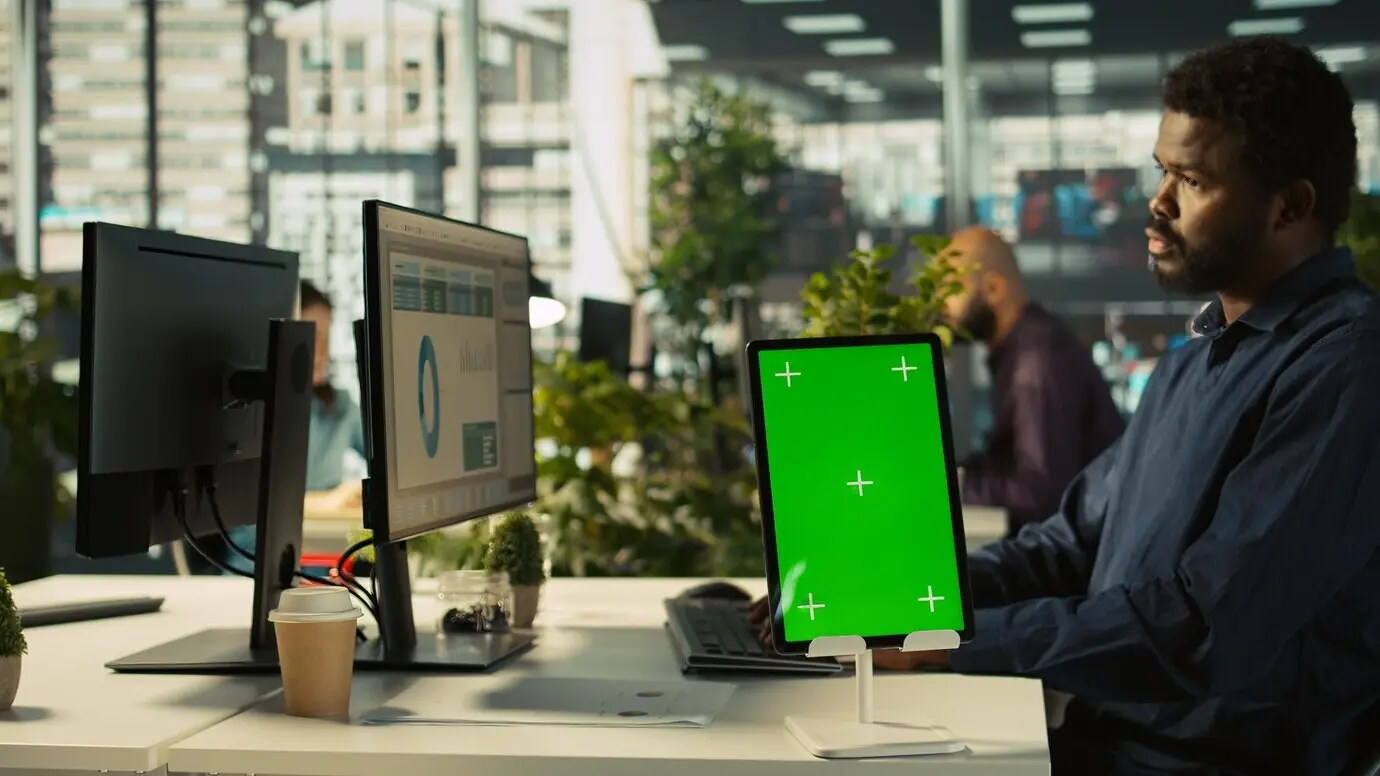 Крупный план планшета с зелёным экраном перед сотрудником в офисе.